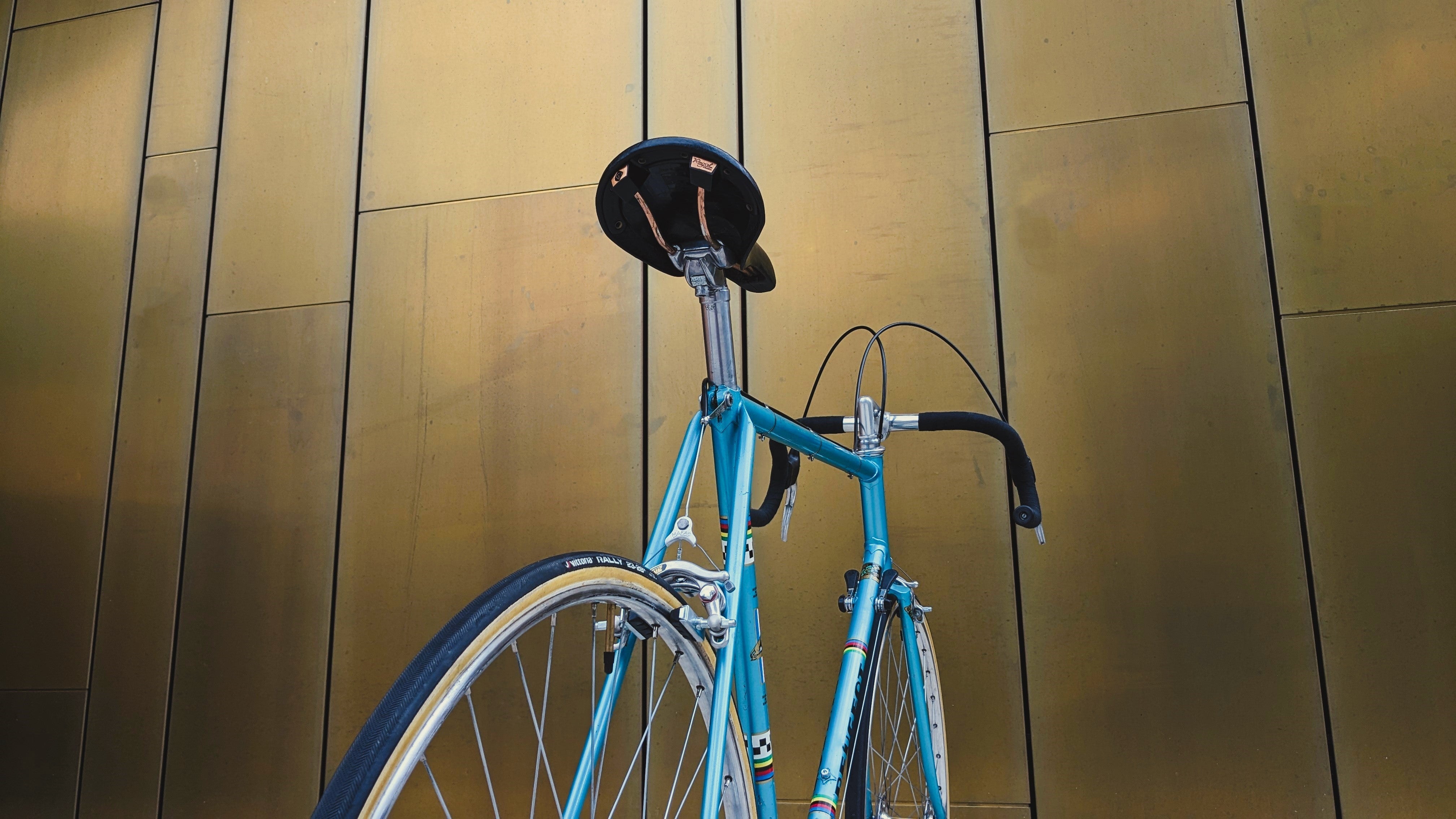 Professional Refurbished Blue Peugeot PX10 Retro Road Bicycle from 1977 standing in front of a golden Steel Wall.